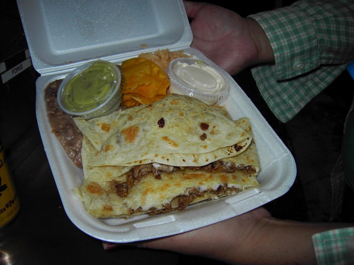A styrofoam box holds a quesadilla, chips, beans, and sauce.