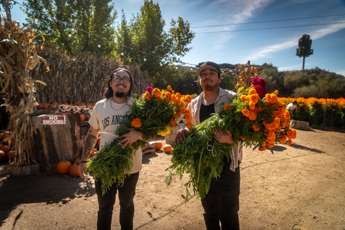 Two men pose while carrying bundles of flowers