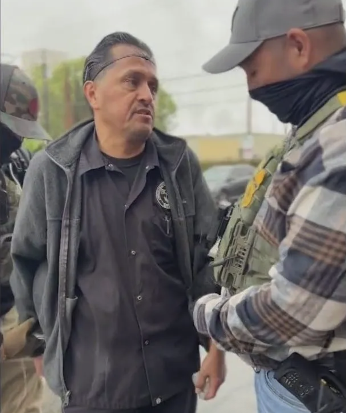 A man in a hair net is detained by a government official wearing a mask.