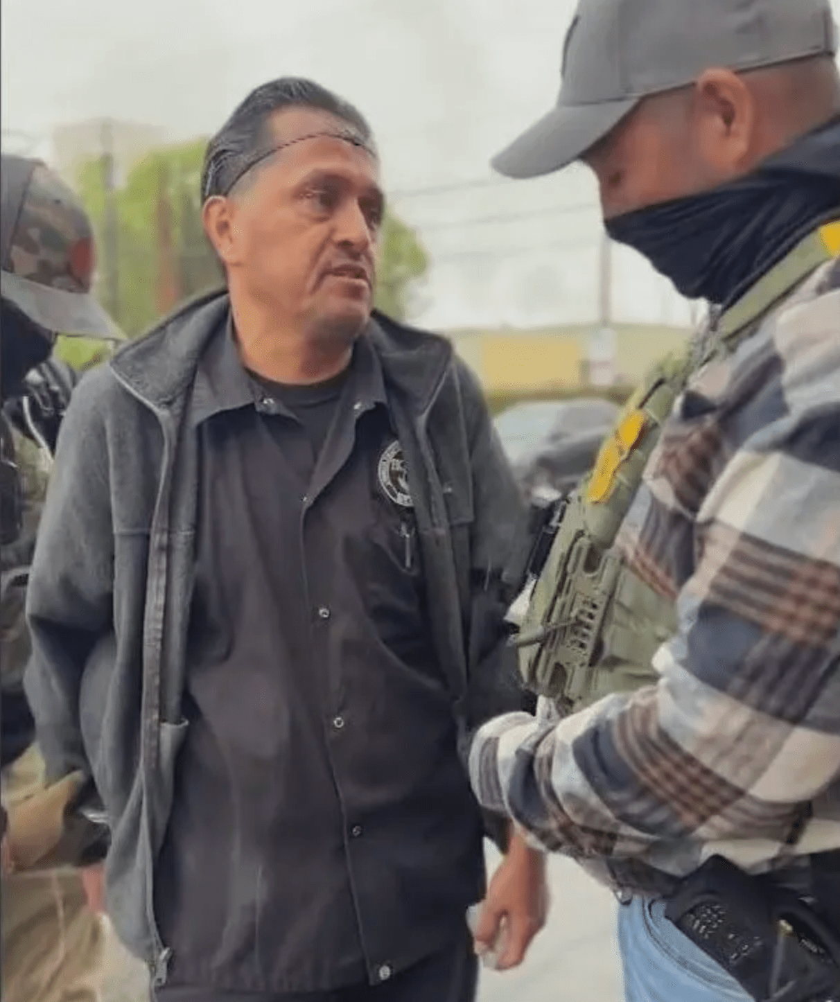 A man in a hair net is detained by a government official wearing a mask.