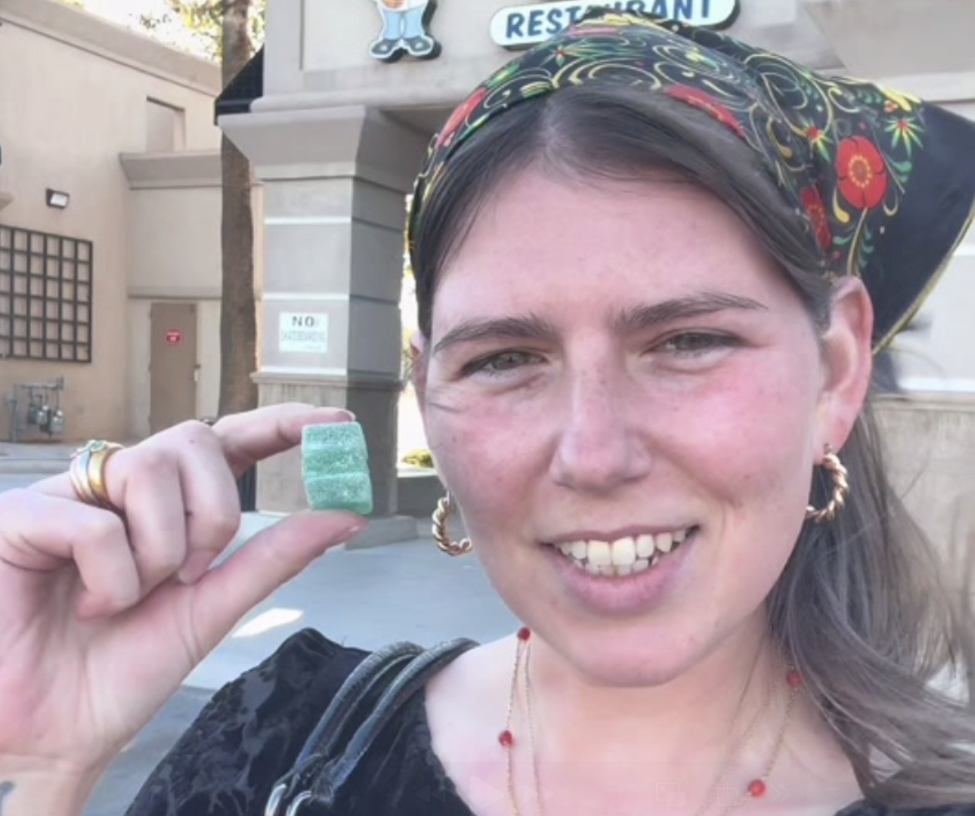 A woman smiles in front of a building while holding green gummies