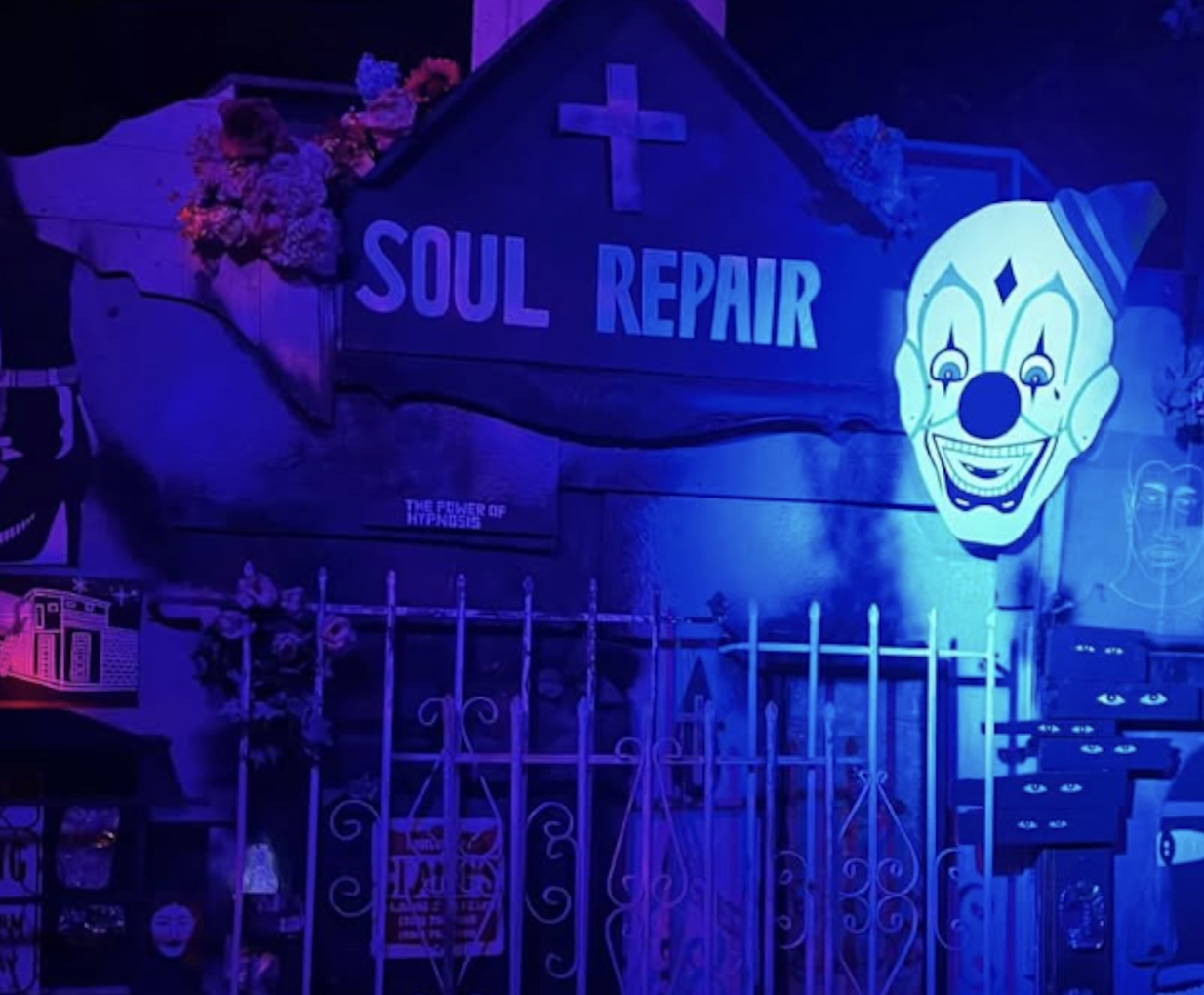 A clown face is plastered on top of a building next to a cross and the words "SOUL REPAIR"