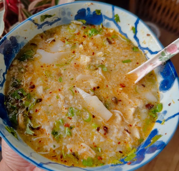 A blue bowl of chicken rice porridge, with a spoon sticking out of it