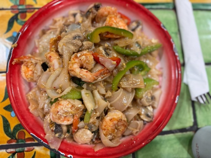 A red bowl of Thai drunken noodles, with shrimp, wide flat noodles, and green bell peppers