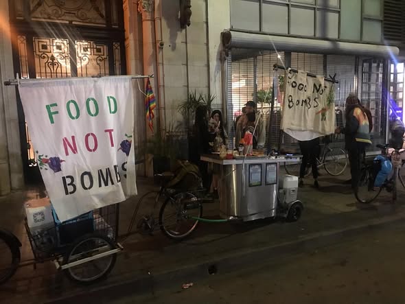 A bike-mounted cart next to two bikes, with signs that say Food Not Bombs