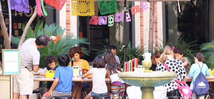 Adults and kids craft outside together at a Dia de los Muertos event.