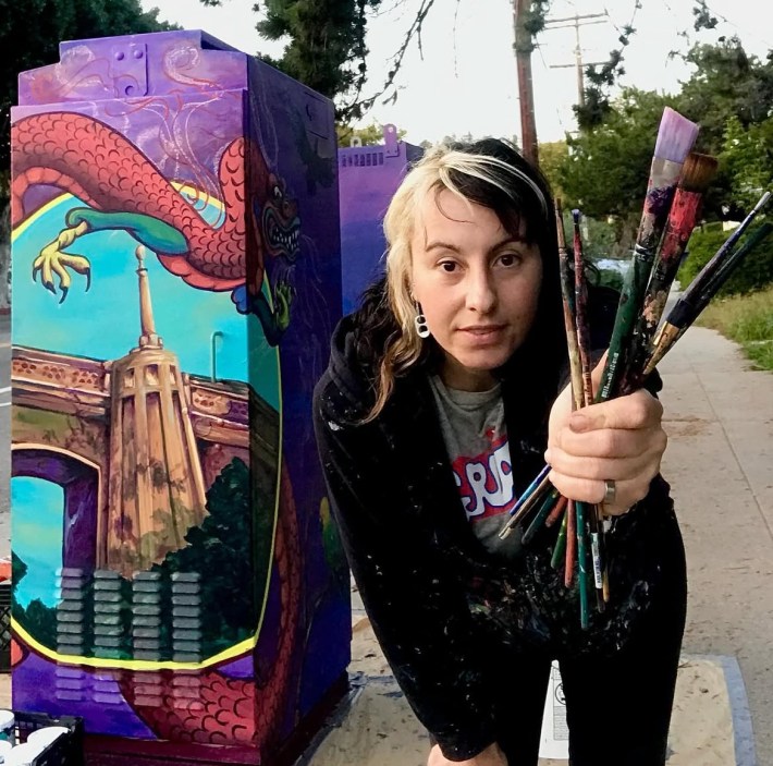 Sol Luongo holding paintbrushes in front of one of her murals.