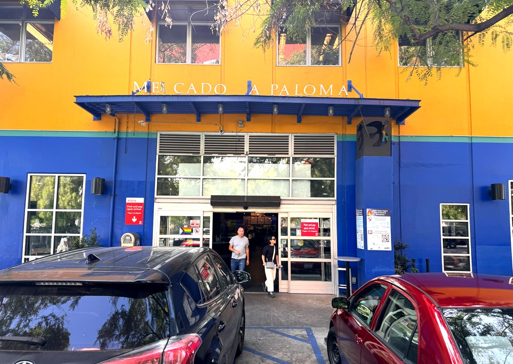 An exterior shot of Mercado de Paloma in Los Angeles, with two people leaving its big blue entrance