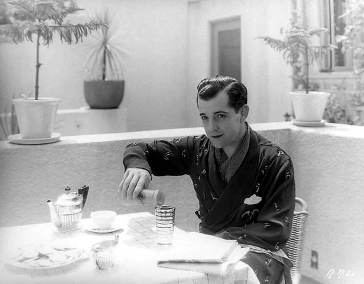 Ramon Novarro enjoys an outdoor breakfast while wearing a robe.