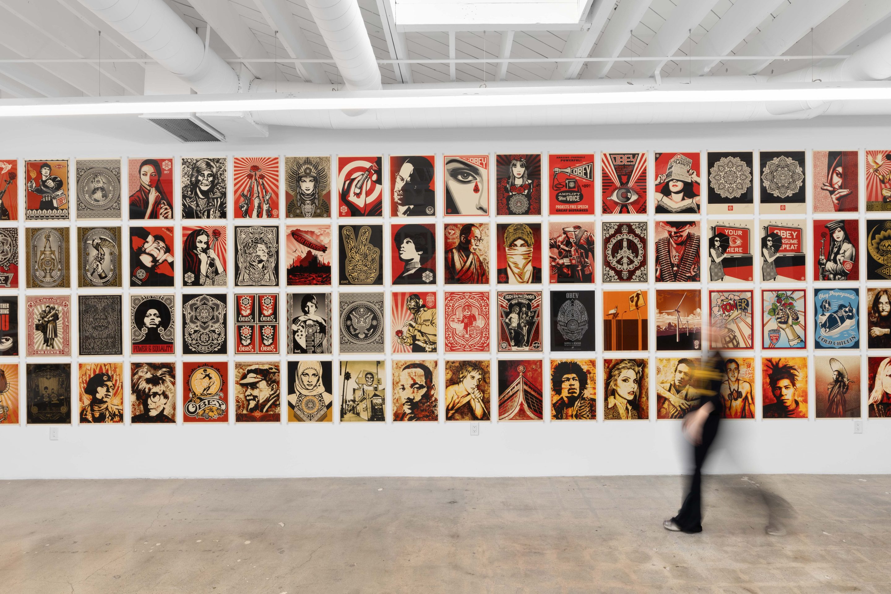 a blurred person walks in front of a wall fully displaying artwork