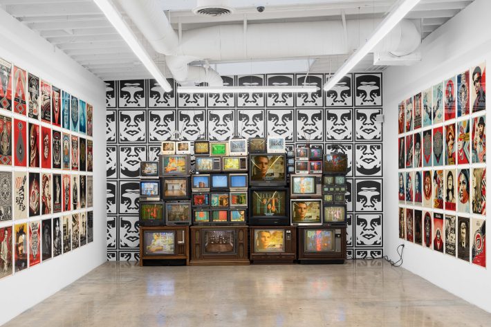 art in front of a wallpaper of the "OBEY" logo printed over and over