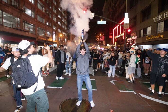 A man in the middle of a crowd holds a firework above his head