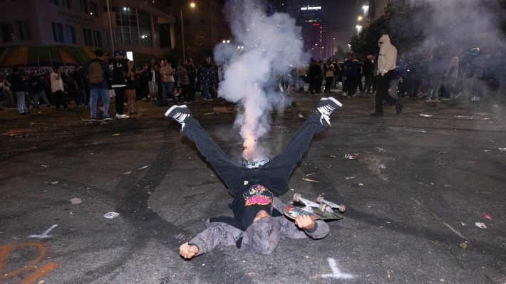 A man poses with his legs spread beneath a firework