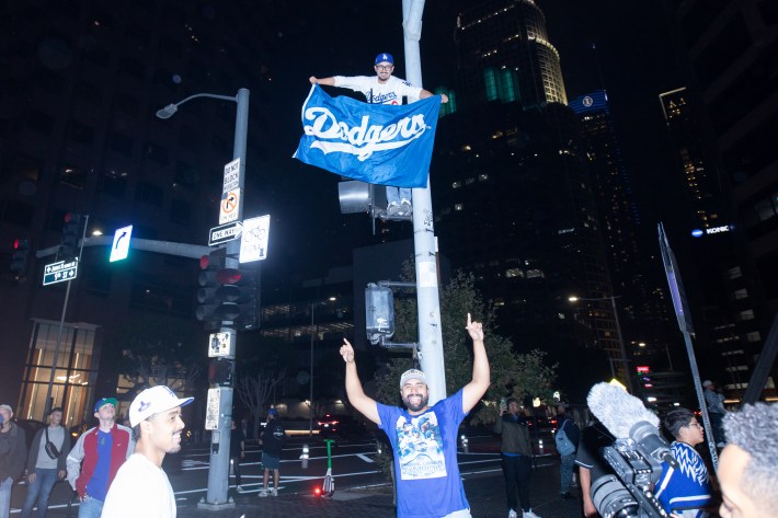 A man stands from atop a post, holding a Dodgers banner