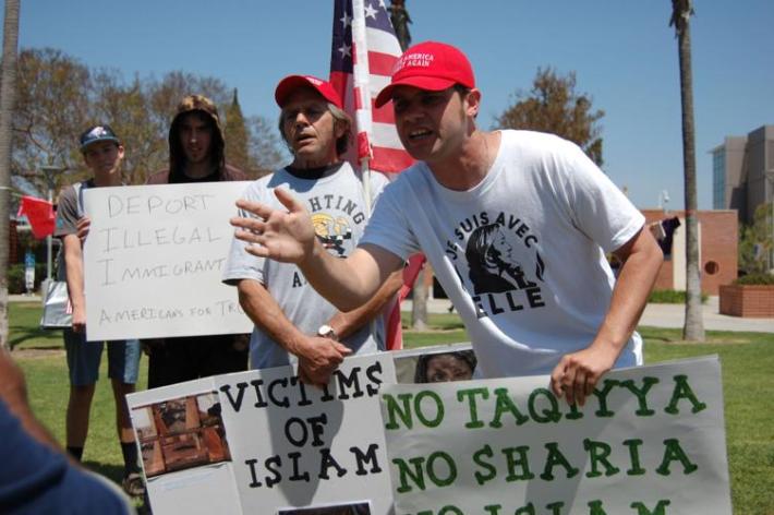 two men spout information in a college quad, holding signs depicting hate speech