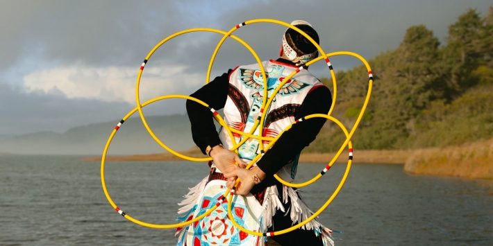 a man in regalia performs a hoop dance