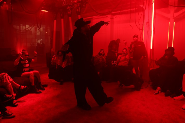 A man is in the center of a circle of people in a red-lit room