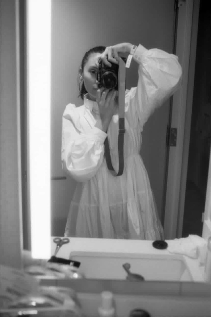 a woman takes a portrait-style selfie of herself using a professional camera. it is a black and white image