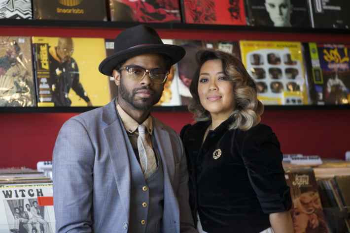 a man and woman in dapper attire pose in front of records