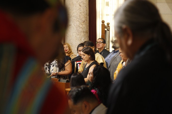 a woman stands at a podium, speaking into a microphone