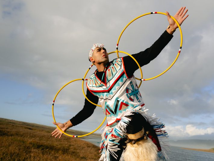 a man hoop dances in regalia while outdoors
