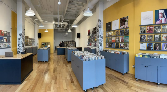 a room with yellow walls and indigo carts. the carts are full of vinyl records for sale. some records are displayed on the wall.
