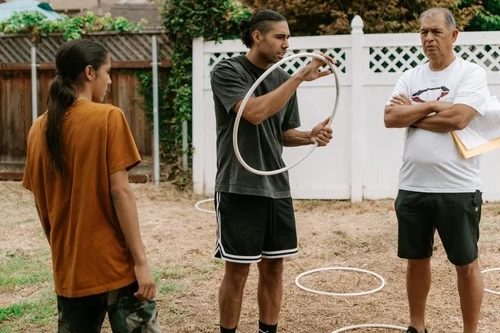 a man (middle) teaches hoop dancing to two students, one young and one older
