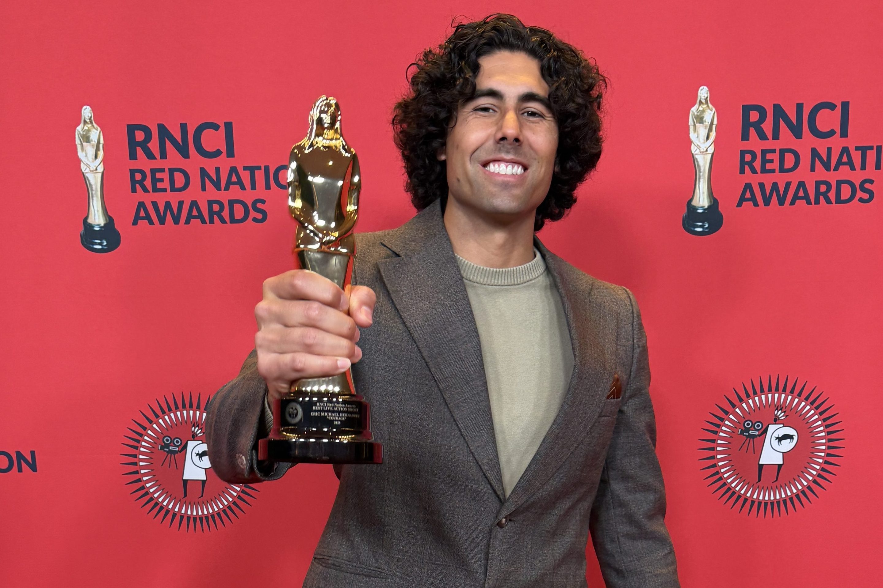 a man in a suit on a red carpet smiles while holding a reward