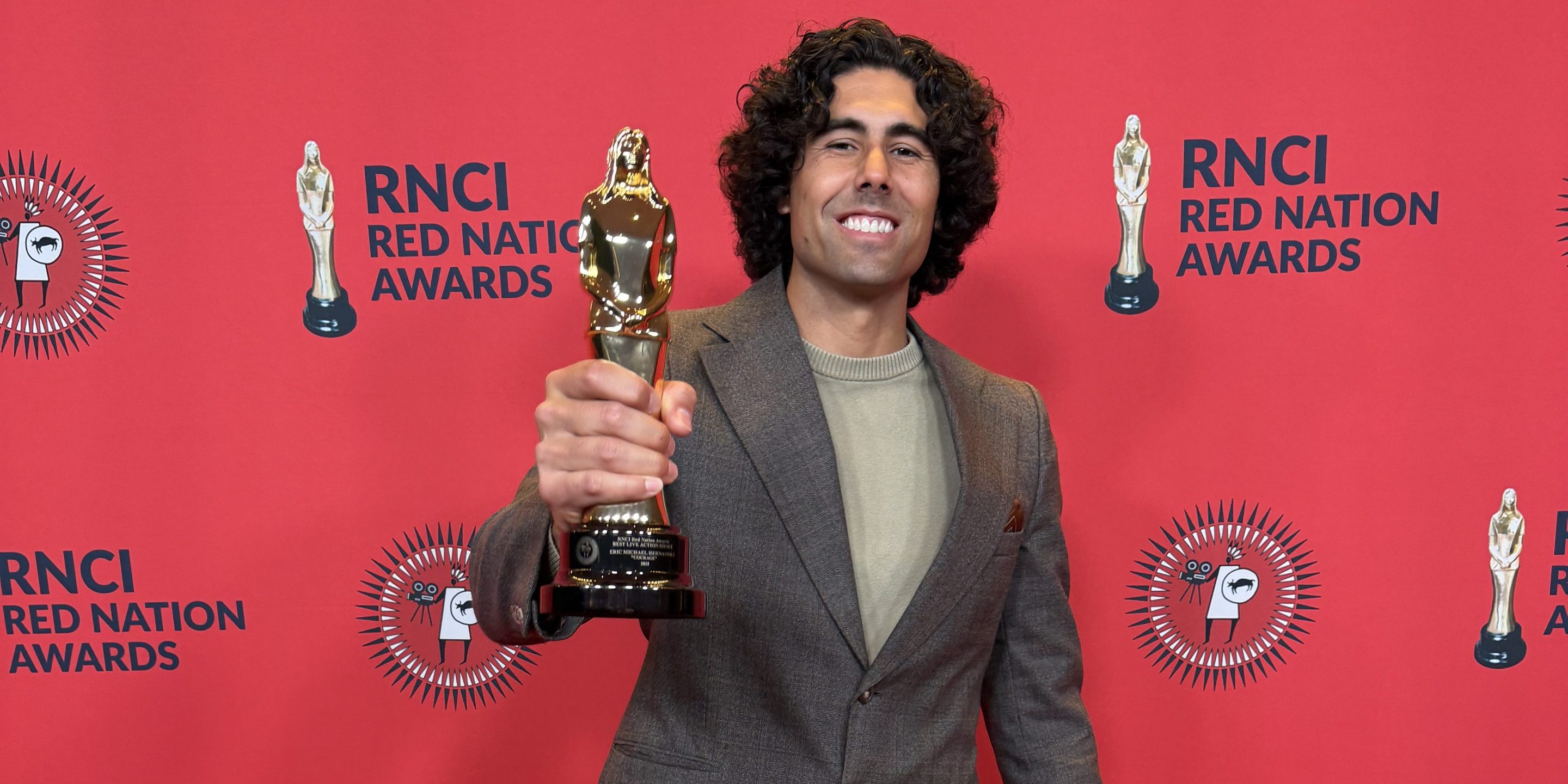 a man in a suit on a red carpet smiles while holding a reward