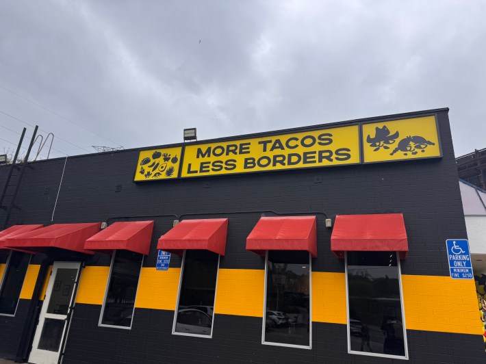 a restaurant building exterior. a large sign says "more tacos less borders"