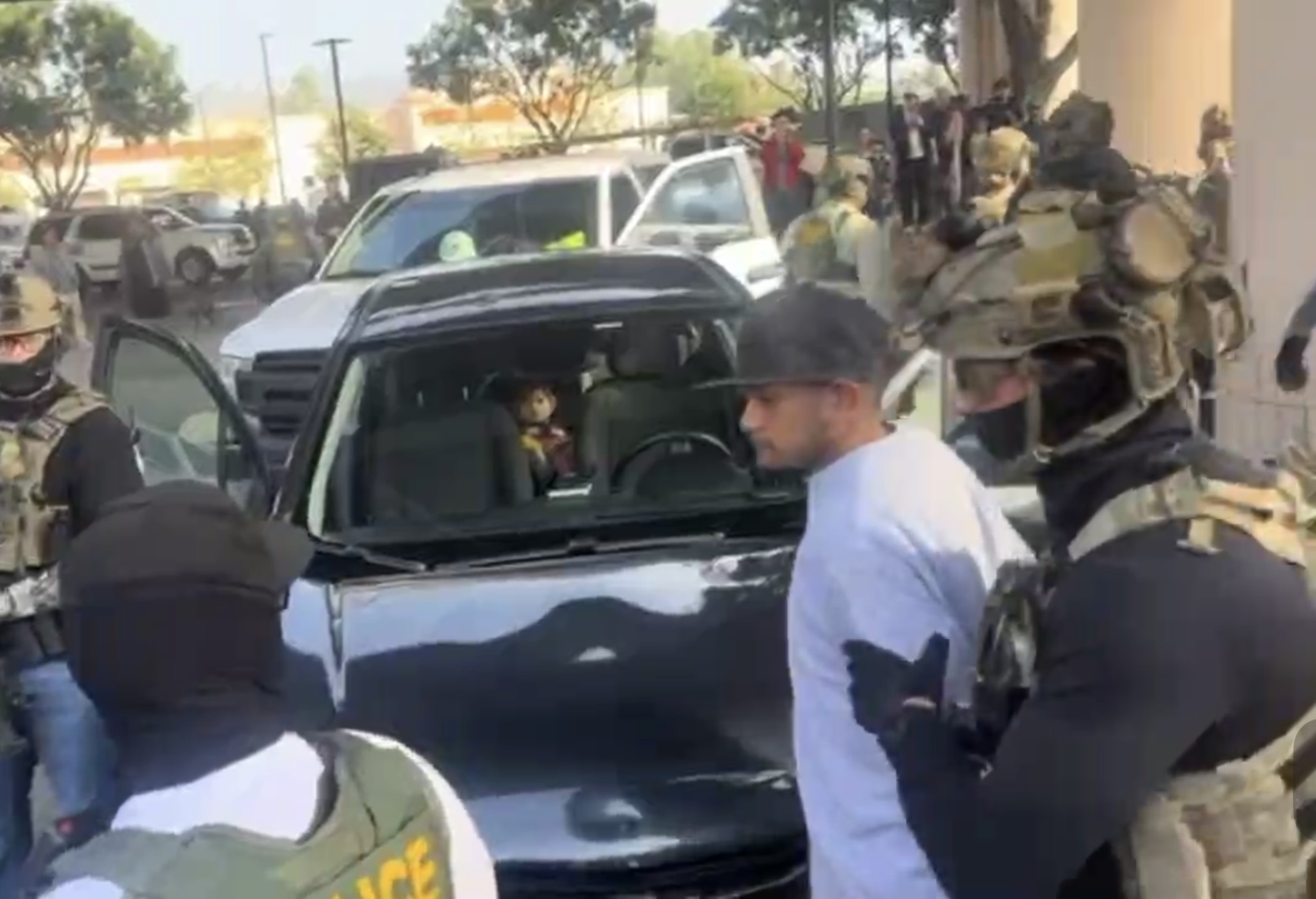 A man is taken into Border Patrol custody while a child looks on from the backseat of a car
