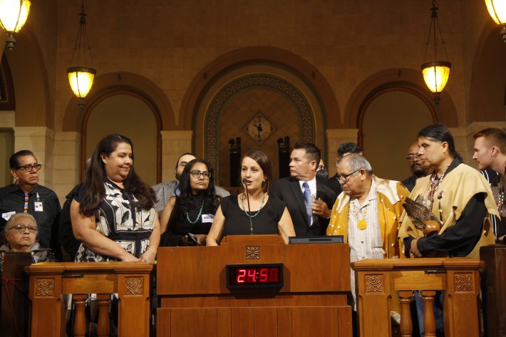 a group of people watch a woman as she speaks from behind a podium