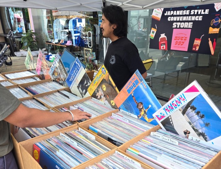 An outdoor Japanese record stand, with its owner behind the records, talking with customers