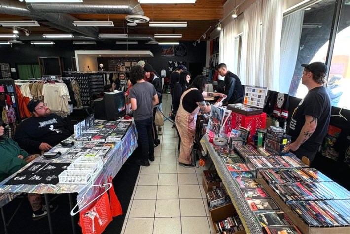 vendors sell items in a record store. patrons browse through merchandise like posters and DVDs