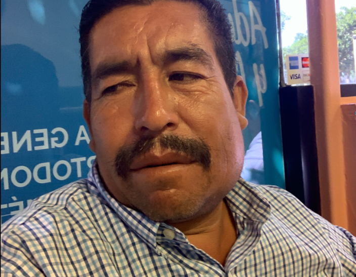 A mustached man looks to his right, in a checkered dress shirt