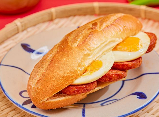A banh mi with hard boiled egg slices and SPAM, on a white and blue plate