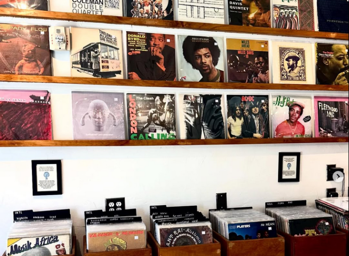 a wall of record covers on display above boxes holding records for sell