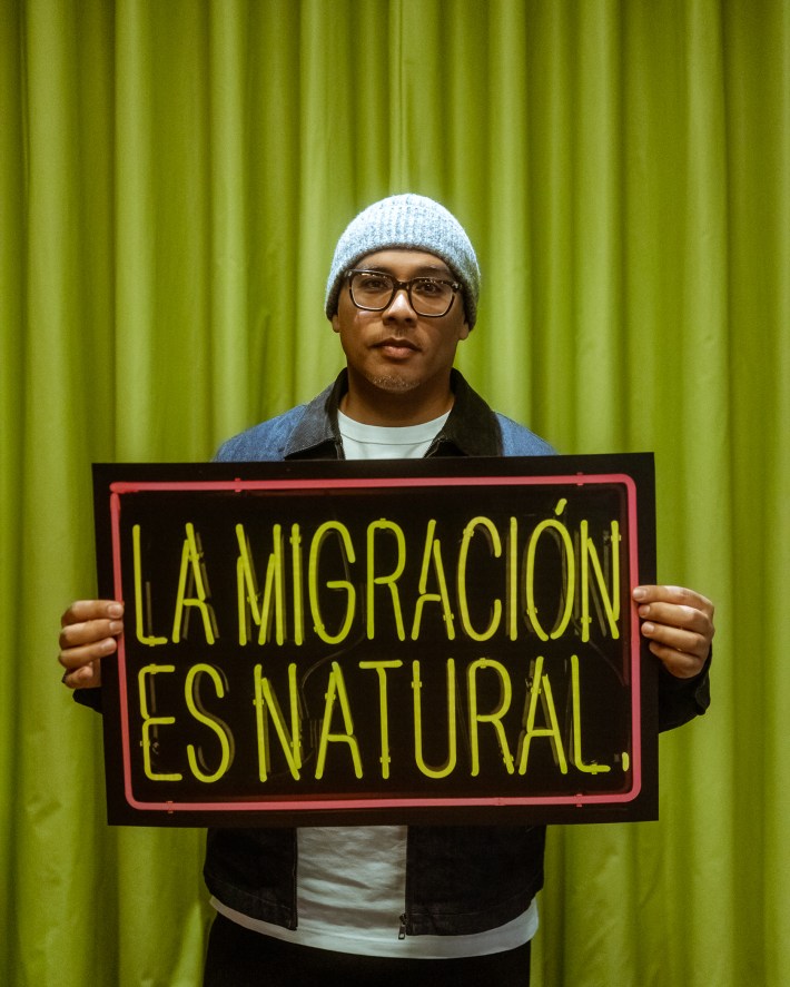 a man holds a poster that says "La Migracion Es Natural."