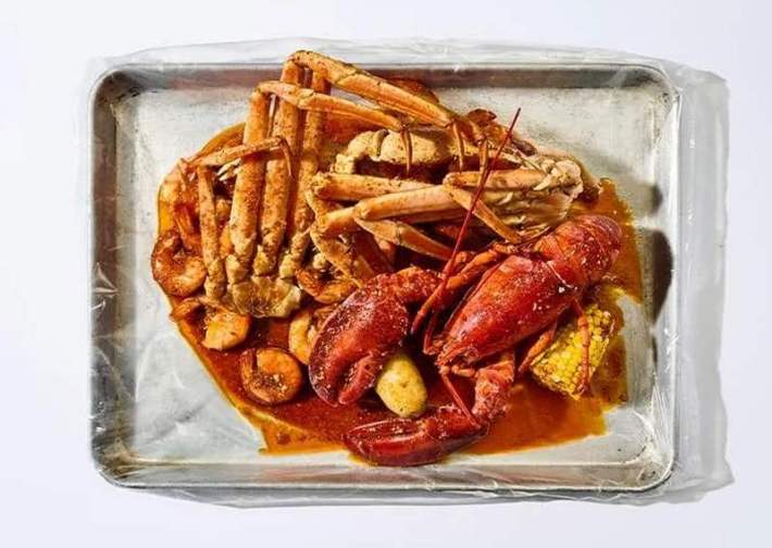 A silver tray loaded with crab legs, lobster, and corn in a slurry of Cajun red sauce