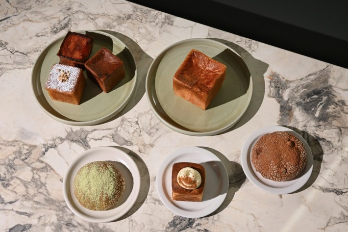 A marble table with a spread of Japanese breads and pastries, including mou and toasts