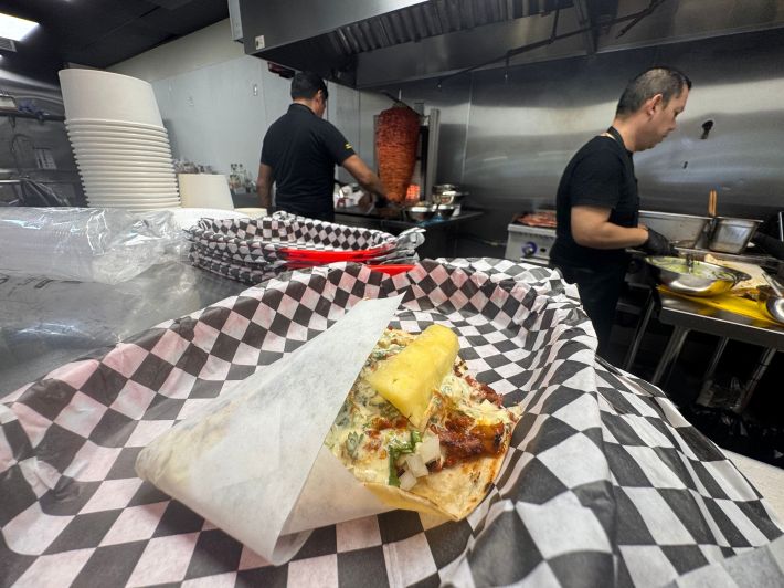men in a kitchen with a taco on a counter in the forefront