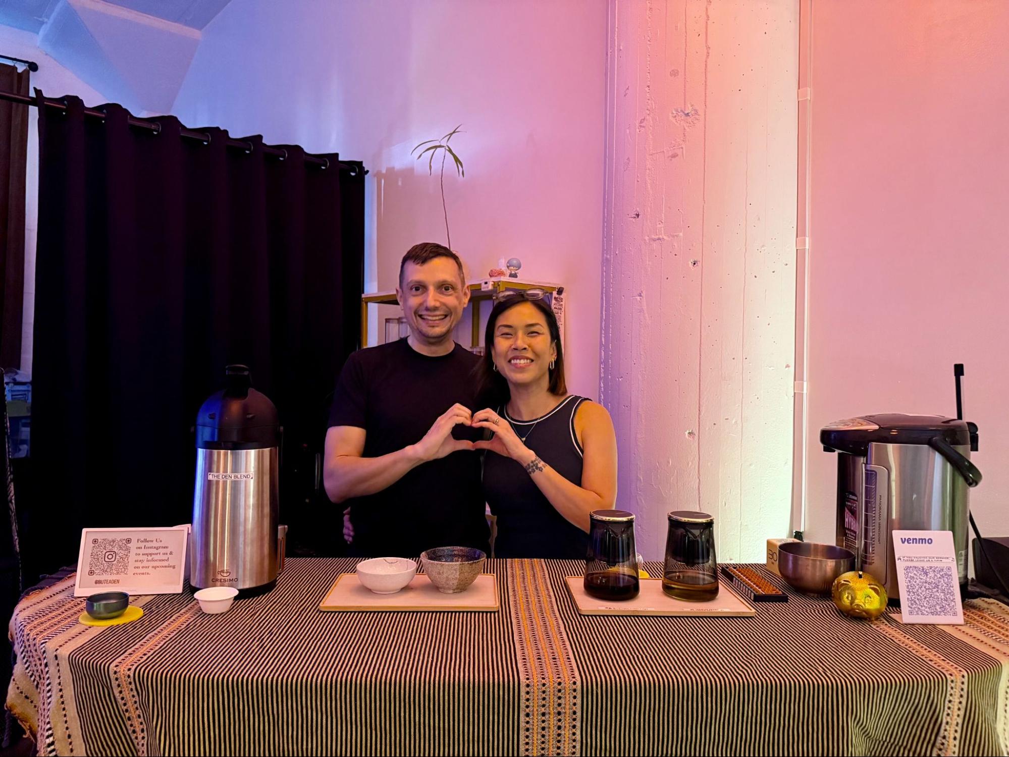 a man and woman, a couple, pose together from behind their tea stand