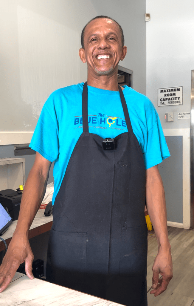 a man in a blue shirt and black apron smiles widely