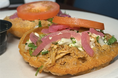 An open-faced puffy taco with meat, onions, and tomatoes on top