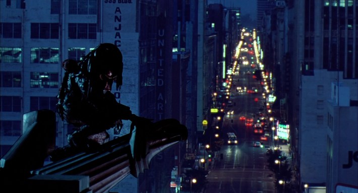 a monster perches on top of a tall building overlooking a city street