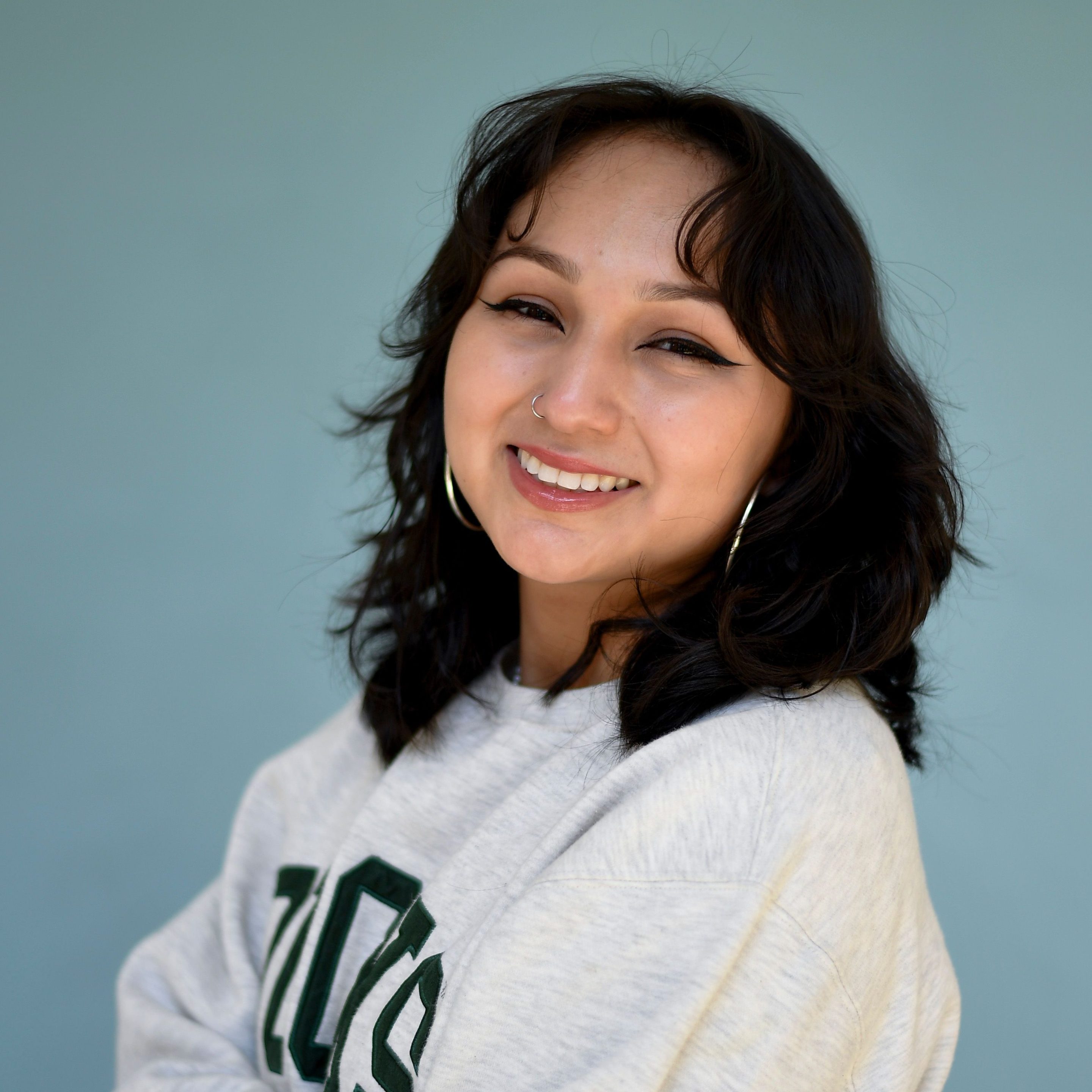 a girl smiles into the camera in front of a blue background