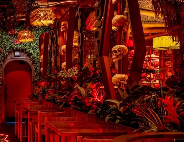 A tiki bar in red light with fake skulls on the walls
