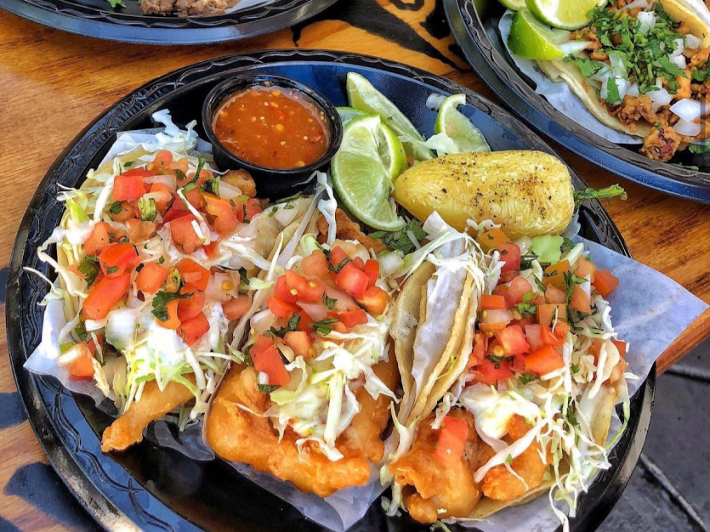 Taco Nazo's famous fish tacos served on a plate with red salsa and a Anaheim chile.