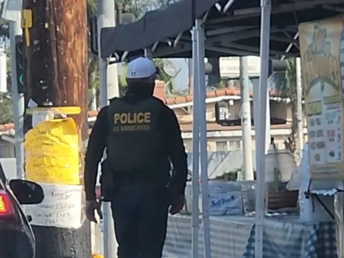 an armed border patrol agent lurks near a food stand on the sidewalk
