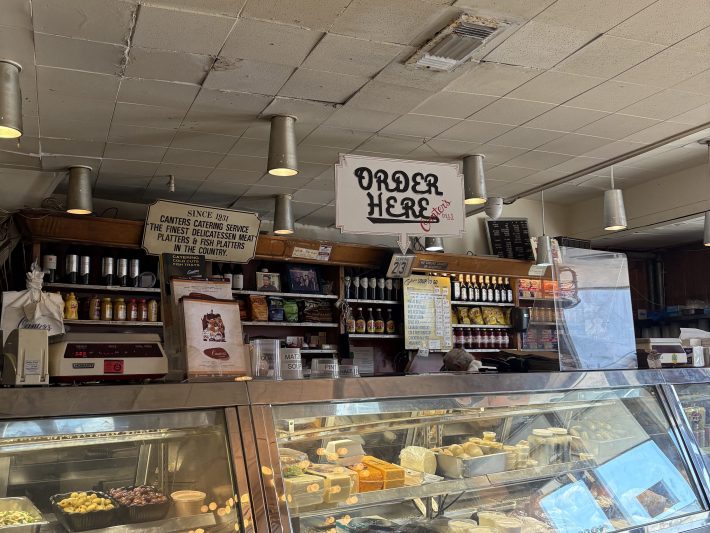 an interior of a deli, showing the "order here" sign and the display case of food